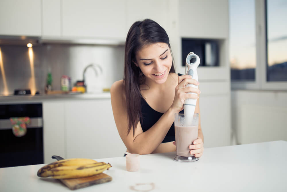 Mladá žena v čiernom tope, ktorá si pripravuje proteínový nápoj s rozmixovaným banánom